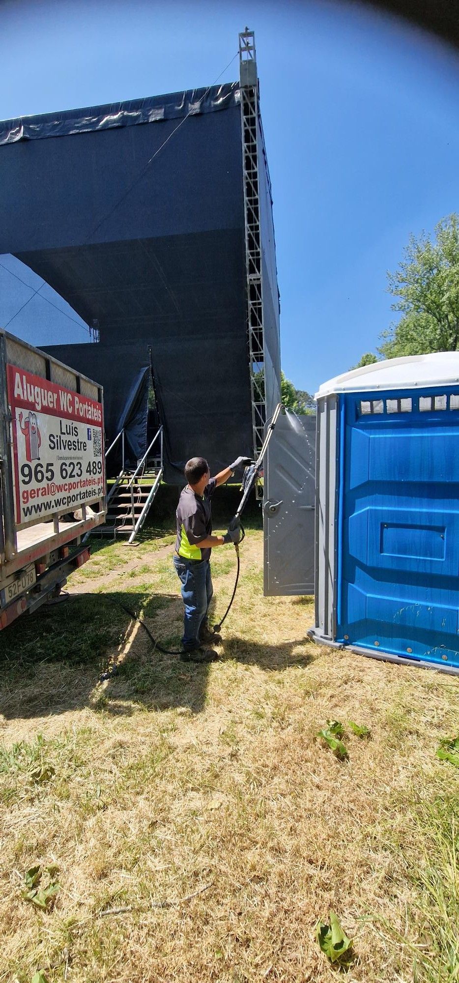 Técnico a lavar a porta de um WC portátil junto a um palco
