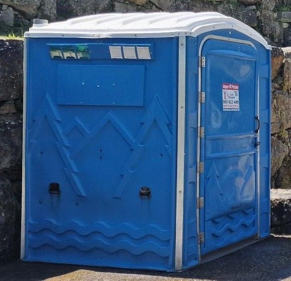 Cabina WC ampla azul instalada junto a um muro de pedra