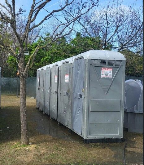 Fila de cinco WC portáteis cinzentos num recinto